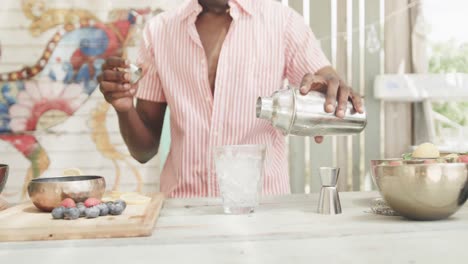 Midsection-of-african-american-barman-pouring-cocktail-behind-the-counter-at-beach-bar,-slow-motion