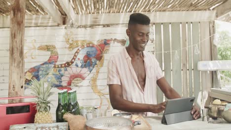 Happy-african-american-barman-using-tablet-behind-the-counter-at-beach-bar,-slow-motion