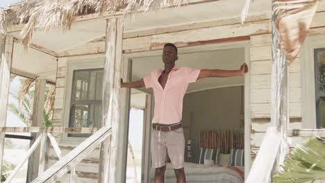 African-american-man-stretching-on-the-porch-of-wooden-beach-house-in-the-morning-sun,-slow-motion
