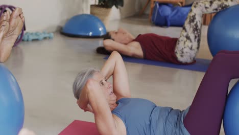 Focused-diverse-seniors-using-exercise-balls-in-pilates-class,-unaltered,-in-slow-motion