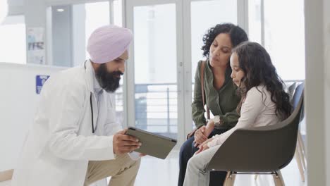 Biracial-Sikh-Arzt-Im-Turban-Mit-Tablet-Im-Gespräch-Mit-Mädchen-Und-Mutter-Im-Krankenhaus,-Zeitlupe