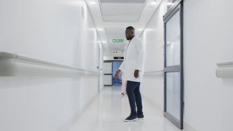 Stressed-african-american-male-doctor-leaning-on-wall-in-hospital-in-slow-motion