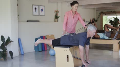 Focused-senior-caucasian-man-exercising-with-female-pilates-coach,-unaltered,-in-slow-motion