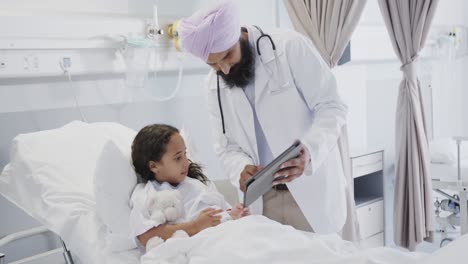 Happy-biracial-doctor-using-tablet-with-sick-girl-patient-in-hospital-bed-in-slow-motion