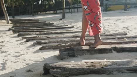 Low-section-of-biracial-woman-in-red-dress-walking-barefoot-on-boardwalk-on-sunny-beach,-slow-motion