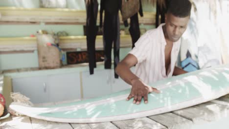 African-american-man-preparing-surfboard-on-the-counter-of-surf-rental-beach-shack,-slow-motion