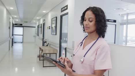 Portrait-of-happy-biracial-female-doctor-using-tablet-in-hospital-in-slow-motion
