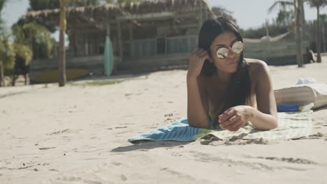 Fröhliche-Hispanische-Frau-Mit-Sonnenbrille,-Die-Am-Strand-In-Der-Sonne-Liegt,-Kopierraum,-Zeitlupe