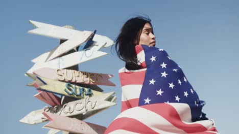 Happy-hispanic-woman-dancing-with-american-flag-by-signpost-on-sunny-beach,-slow-motion
