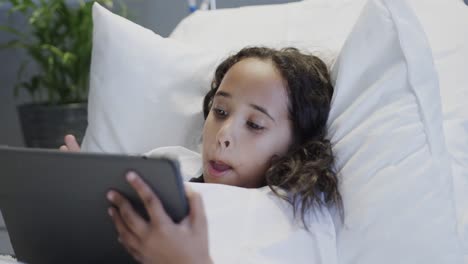 Happy-biracial-sick-girl-patient-using-tablet-in-hospital-bed-in-slow-motion