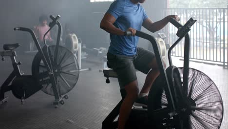 Focused-biracial-man-training-on-elliptical-bike-at-gym,-slow-motion