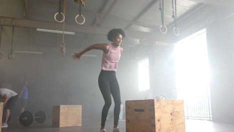 Focused-african-american-woman-jumping-onto-box,-cross-training-at-gym,-in-slow-motion