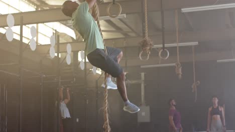 Biracial-man-training-at-gym-climbing-rope,-in-slow-motion