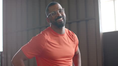 Porträt-Eines-Glücklichen-Afroamerikanischen-Mannes-Mit-Brille,-Der-Im-Fitnessstudio-In-Die-Kamera-Lächelt,-In-Zeitlupe