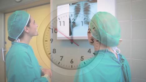 Animation-Der-Tickenden-Uhr-über-Zwei-Verschiedene-Chirurginnen,-Die-Im-Krankenhaus-über-Einen-Röntgenbericht-Diskutieren