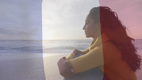Animation-Der-Flagge-Frankreichs-über-Einer-Biracial-Frau,-Die-Am-Strand-Sitzt