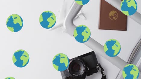 Animation-of-globes-over-suitcase,-passport,-camera-and-plane-model-on-white-background
