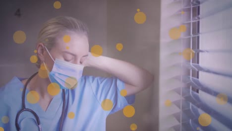 Animation-of-yellow-spots-over-caucasian-female-health-worker-looking-out-of-the-window-at-hospital