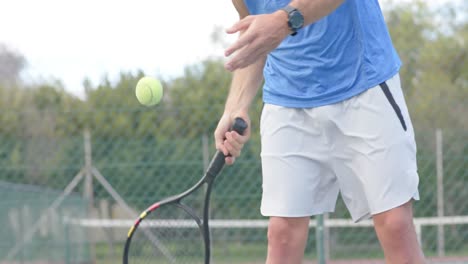Midsection-of-caucasian-male-tennis-player-hitting-ball-with-racket-at-outdoor-court-in-slow-motion