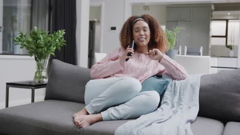 Happy-biracial-woman-relaxing-on-couch-talking-on-smartphone-at-home,-in-slow-motion