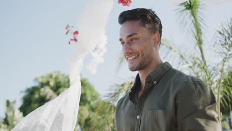 Happy-biracial-groom-smiling-at-his-beach-wedding,-in-slow-motion