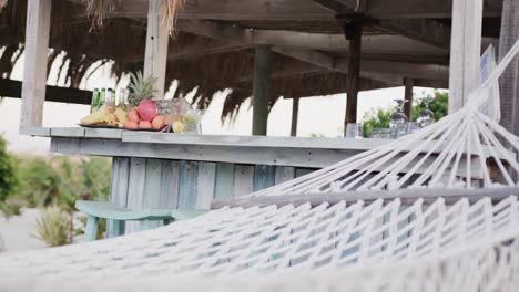 Empty-hammock,-and-fruits-and-drinks-on-counter-at-beach-bar,-in-slow-motion-with-copy-space