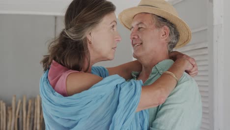 Happy-senior-caucasian-couple-talking-and-embracing-in-holiday-beach-house,-in-slow-motion