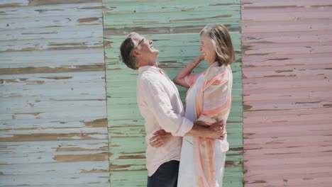 Happy-senior-caucasian-couple-embracing-by-coloured-weathered-wooden-wall,-in-slow-motion
