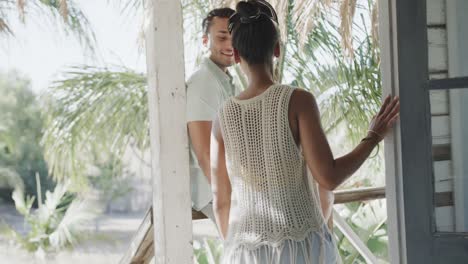 Happy-diverse-couple-talking-and-embracing-on-sunny-beach-house-porch,-in-slow-motion