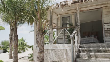 Exterior-of-wooden-holiday-beach-house-on-sunny-tropical-beach-with-palm-trees,-in-slow-motion