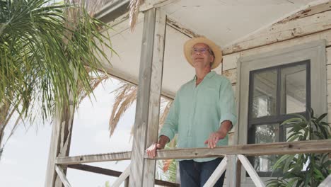 Happy-senior-caucasian-man-standing-on-the-porch-of-wooden-beach-house-enjoying-view,-in-slow-motion