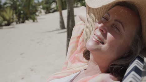 Smiling-senior-caucasian-woman-sitting-in-deckchair-sleeping-on-sunny-beach,-in-slow-motion