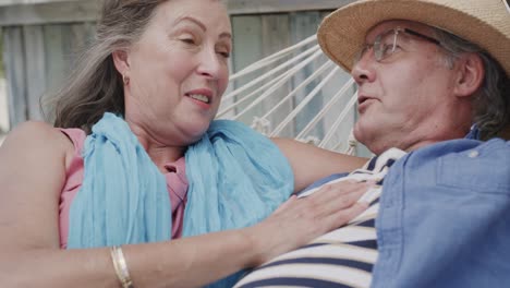 Happy-senior-caucasian-couple-lying-on-hammock-talking-outside-beach-bar,-in-slow-motion