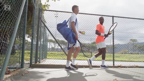 Rear-view-of-diverse-male-tennis-players-walking-and-talking-at-outdoor-court-in-slow-motion