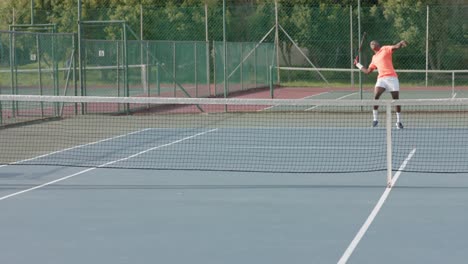 African-american-male-tennis-player-serving-ball-to-opponent-on-outdoor-court-in-slow-motion