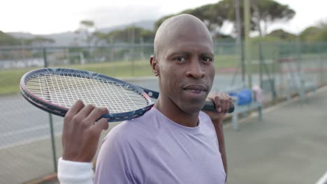 Portrait-of-happy-african-american-male-tennis-player-holding-racket-at-outdoor-court,-slow-motion
