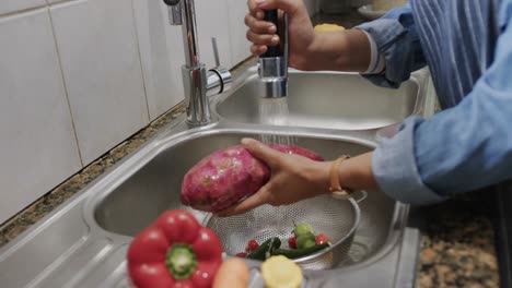 Hände-Einer-Gemischtrassigen-Frau,-Die-Gemüse-In-Der-Küchenspüle-Wäscht,-Zeitlupe