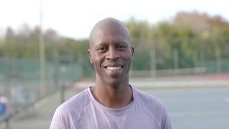 Porträt-Eines-Glücklichen-Afroamerikanischen-Männlichen-Tennisspielers,-Der-Auf-Dem-Außenplatz-Lächelt,-Zeitlupe