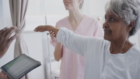 Diverse-male-doctor-with-tablet-and-happy-female-physio-treating-senior-female-patient,-slow-motion