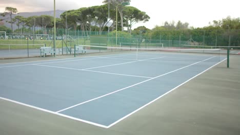 General-view-of-empty-outdoor-tennis-court-surrounded-by-trees,-slow-motion