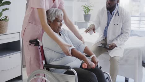 Diverse-male-doctor-and-female-physio-treating-senior-female-patient-in-wheelchair,-slow-motion