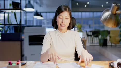 Happy-asian-casual-businesswoman-with-documents-making-video-call,-working-late,-in-slow-motion