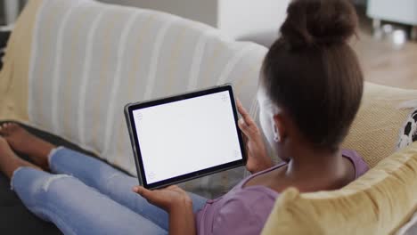 African-american-girl-sitting-on-sofa-and-using-tablet-with-copy-space,-slow-motion