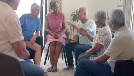 Diversos-Ancianos-Y-Terapeuta-Masculino-Con-Tableta-Hablando-En-Sesión-De-Terapia,-Inalterado,-Cámara-Lenta