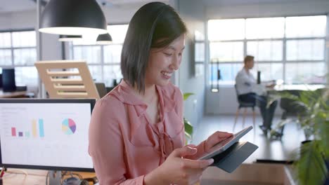 Portrait-of-happy-asian-businesswoman-using-tablet-standing-in-office,-smiling,-in-slow-motion