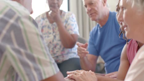 Distressed-diverse-seniors-holding-hands,-talking-in-group-therapy-session,-unaltered,-slow-motion