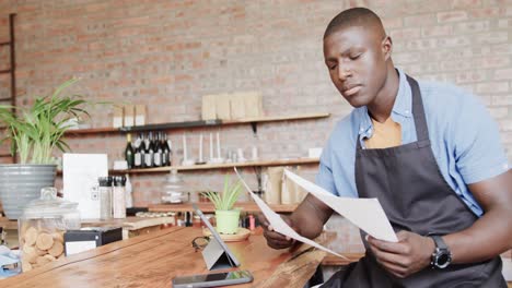 African-american-male-coffee-shop-owner-using-tablet-and-doing-paperwork,-slow-motion