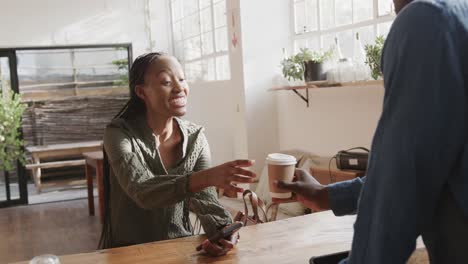 African-american-male-barista-serving-takeaway-coffee-to-happy-female-customer,-slow-motion