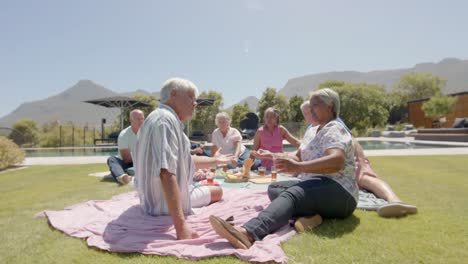 Happy-diverse-senior-friends-having-picnic-and-talking-in-sunny-garden,-unaltered,-in-slow-motion
