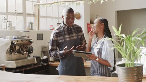 Smiling-african-american-female-and-male-coffee-shop-owners-talking-and-using-tablet,-slow-motion